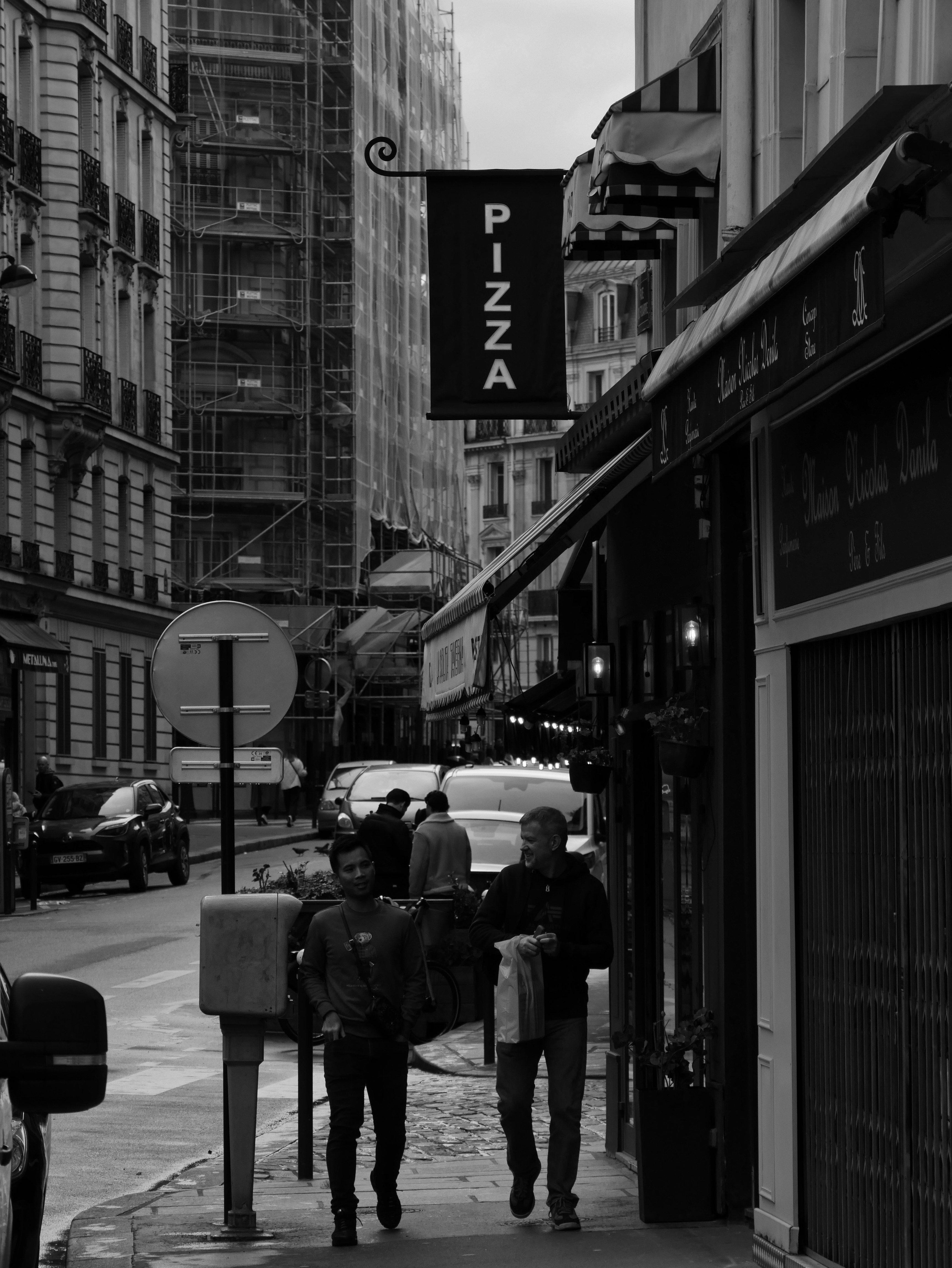 People walk past a pizza restaurant on a city street.